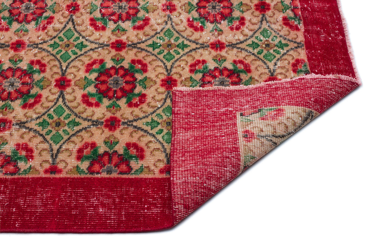 Beige rug with red and green floral medallion pattern and a wide red border, shown with a corner folded over.