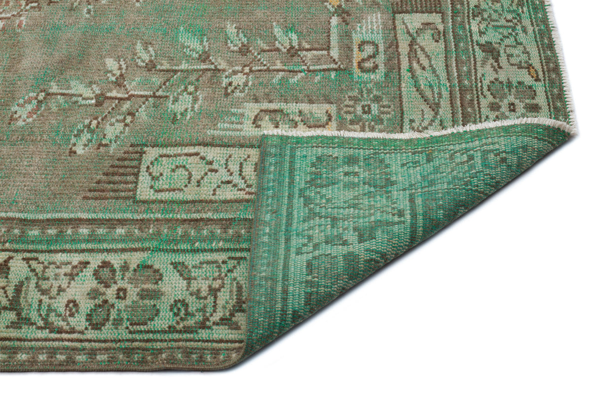 Distressed sage green and brown rug with a traditional floral border and corner fold revealing the woven backing.