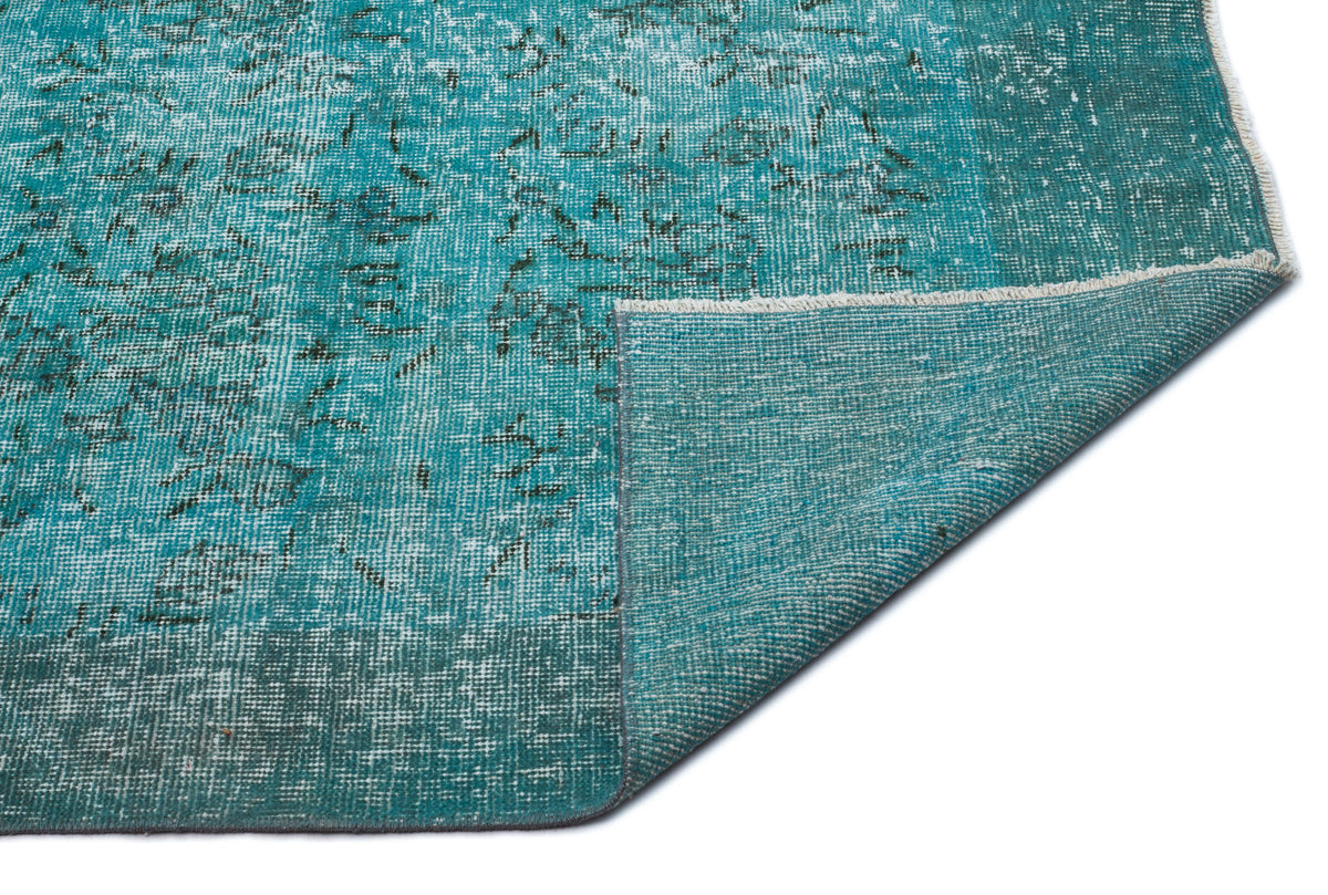Teal distressed area rug with a faded traditional pattern and a folded corner showing the woven backing.