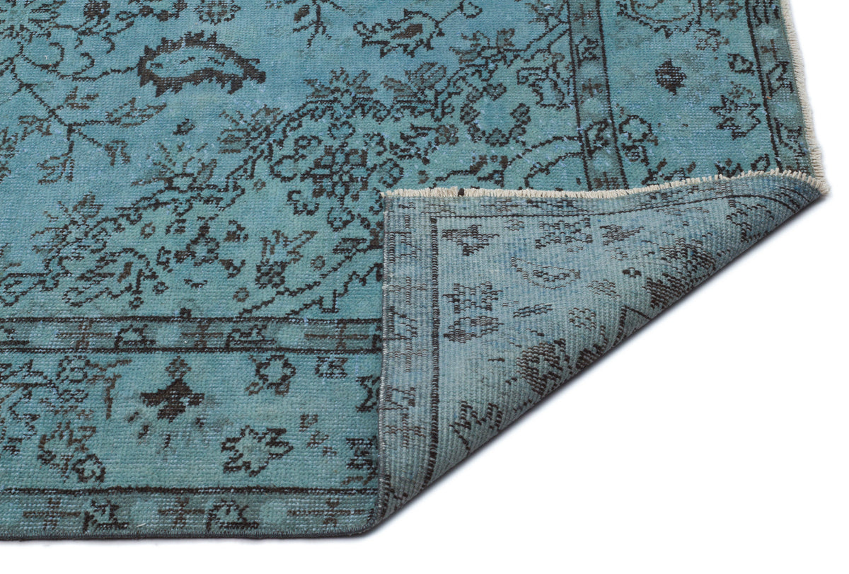 Distressed turquoise rug with a dark charcoal floral pattern and a folded corner, isolated on a white background.