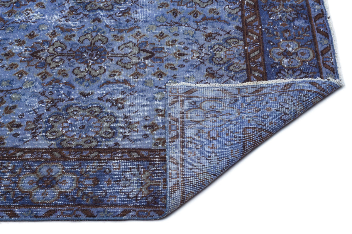 Blue and brown distressed traditional rug with a floral medallion pattern, shown with a corner folded over.