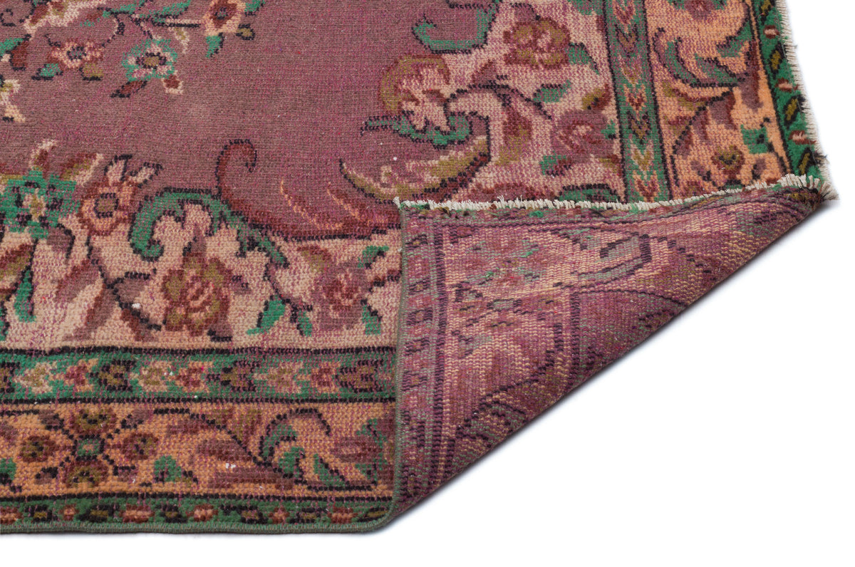 Distressed plum, green, and tan floral patterned rug with a folded corner showing the reverse side.