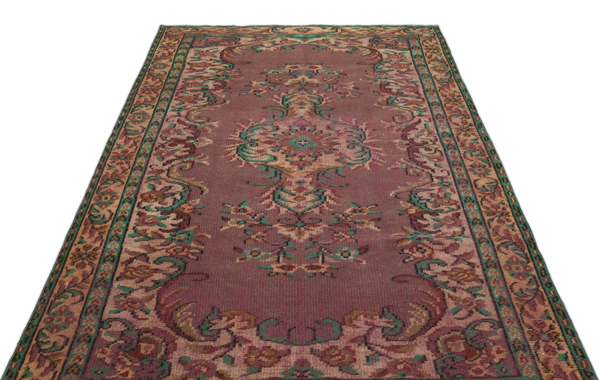 Distressed mauve rug with a central floral medallion and intricate green and tan border patterns on a white background.