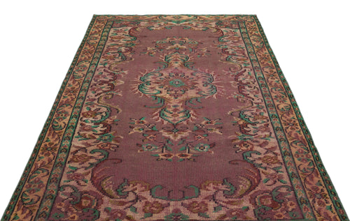 Load image 1 in gallery view. Distressed mauve rug with a central floral medallion and intricate green and tan border patterns on a white background.