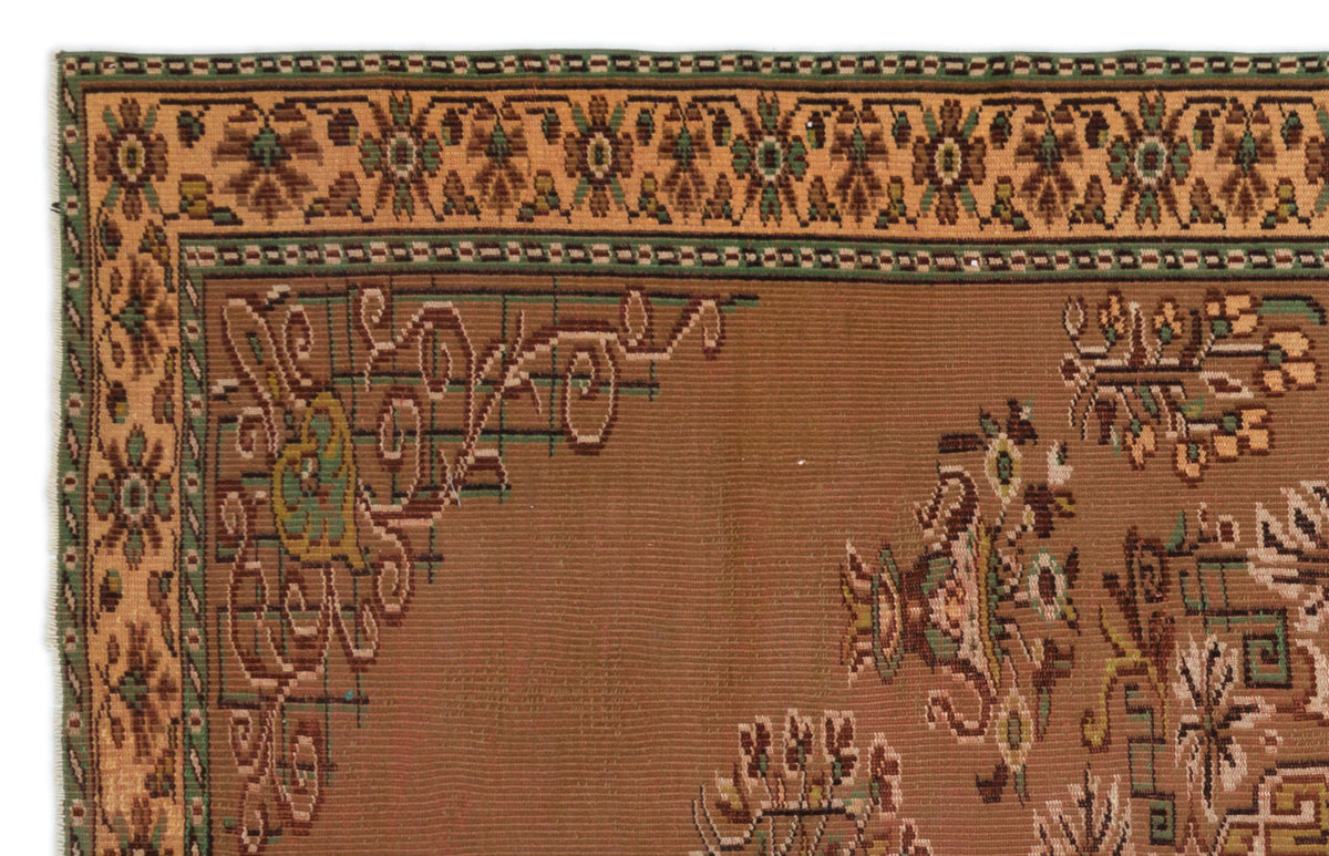 Brown traditional rug with a geometric floral border and central botanical motifs in green, tan, and dark brown.