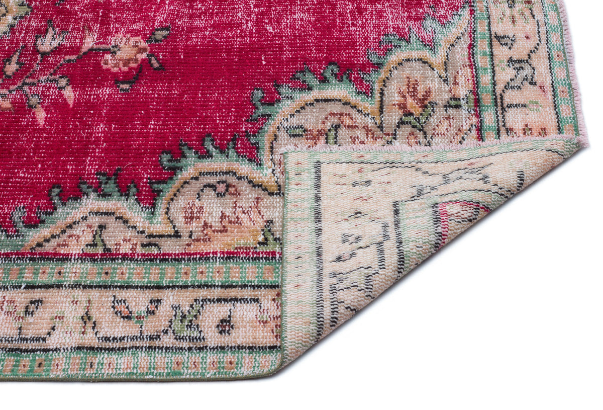 Distressed magenta rug with a floral medallion pattern and beige border, shown with a corner folded over.