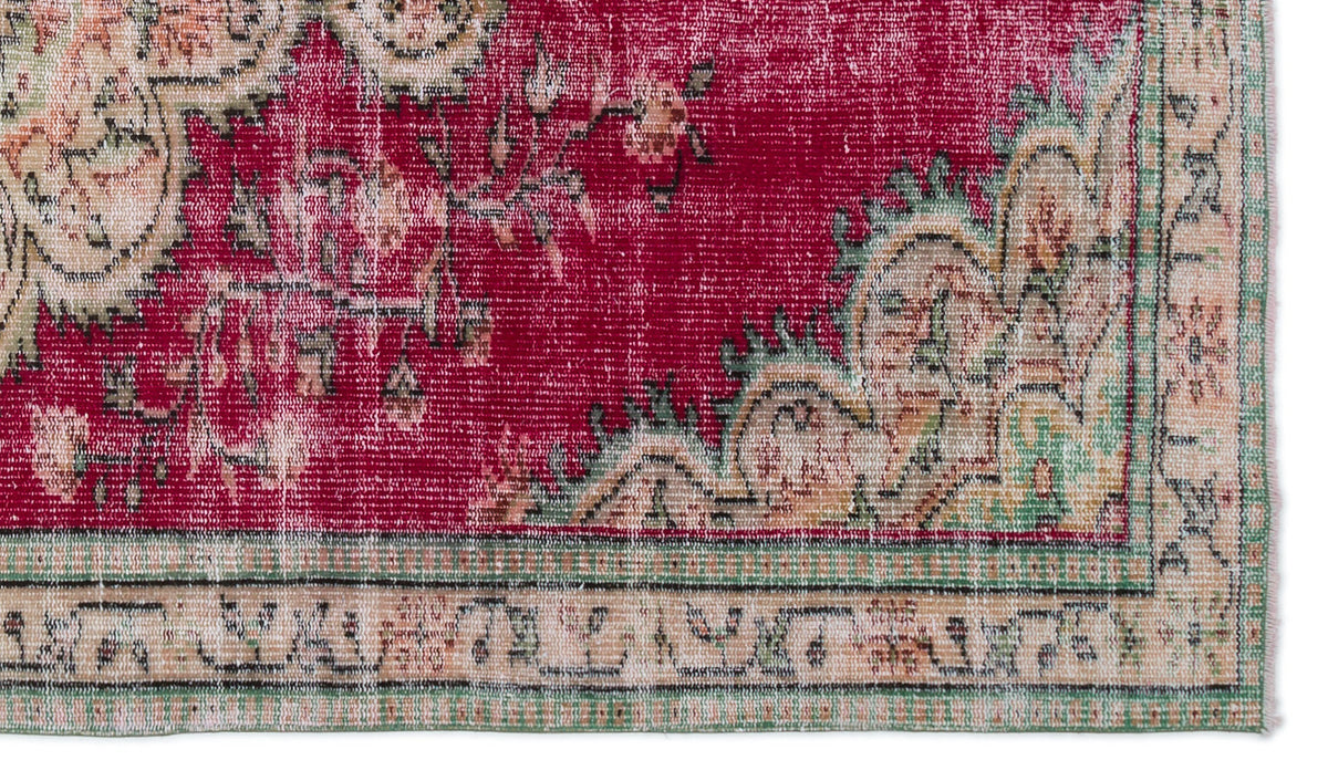Distressed magenta rug with a traditional floral medallion pattern and a beige and green geometric border.