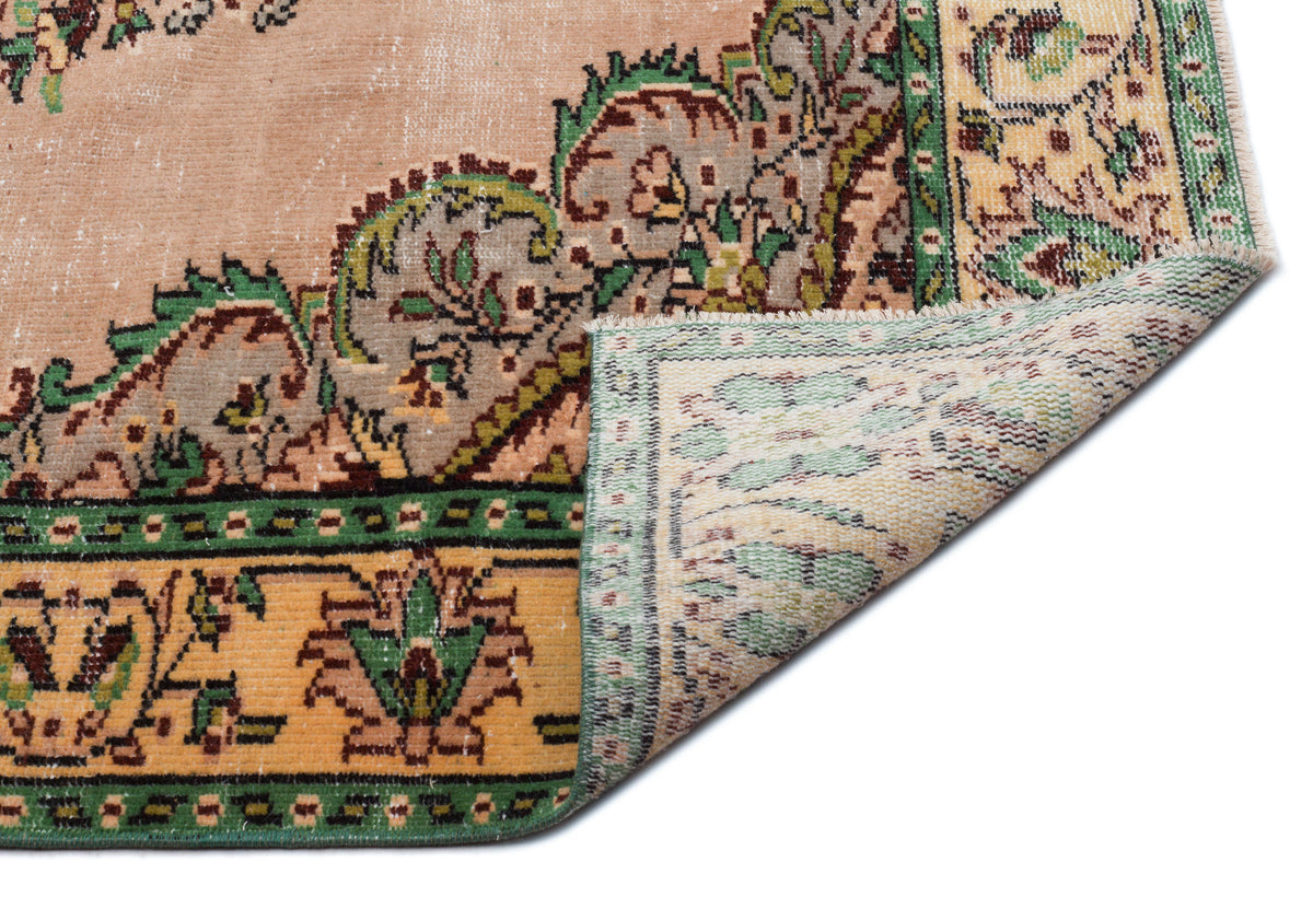 Peach, green, and yellow vintage-style rug with a floral medallion pattern and a folded corner showing the woven backing.