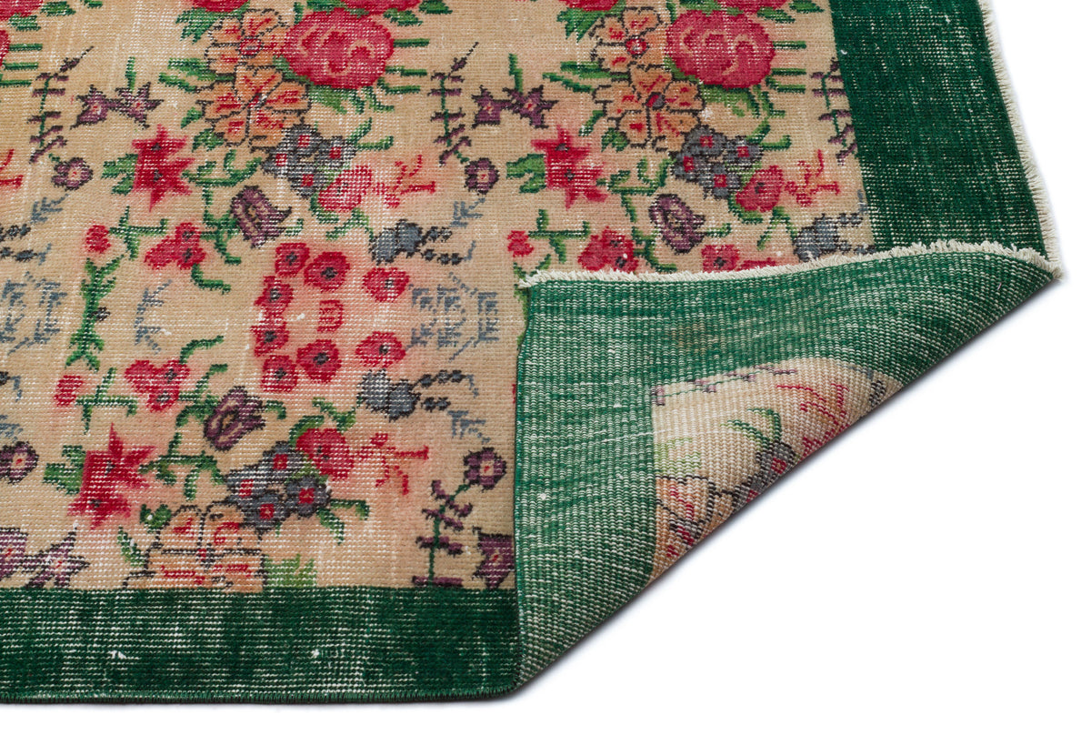 Beige rug with a floral pattern in red, green, and purple, featuring a wide dark green border and a folded corner.