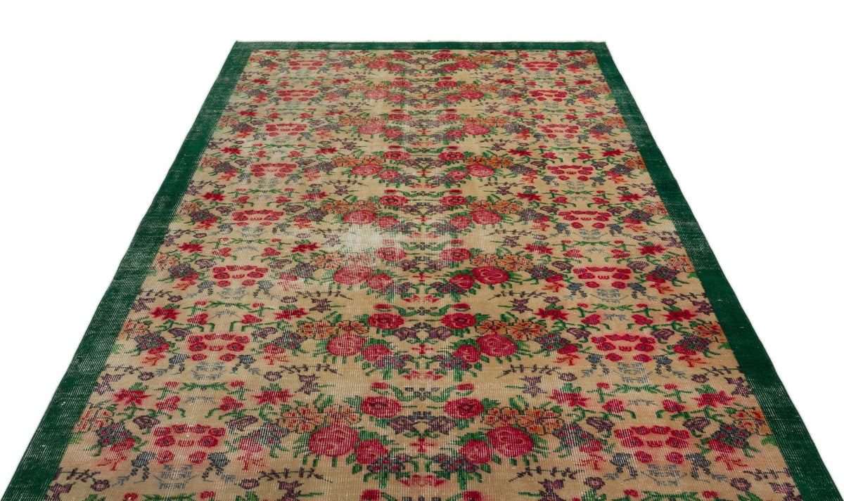Beige vintage-style rug with a distressed floral pattern in red, green, and purple, featuring a solid green border.