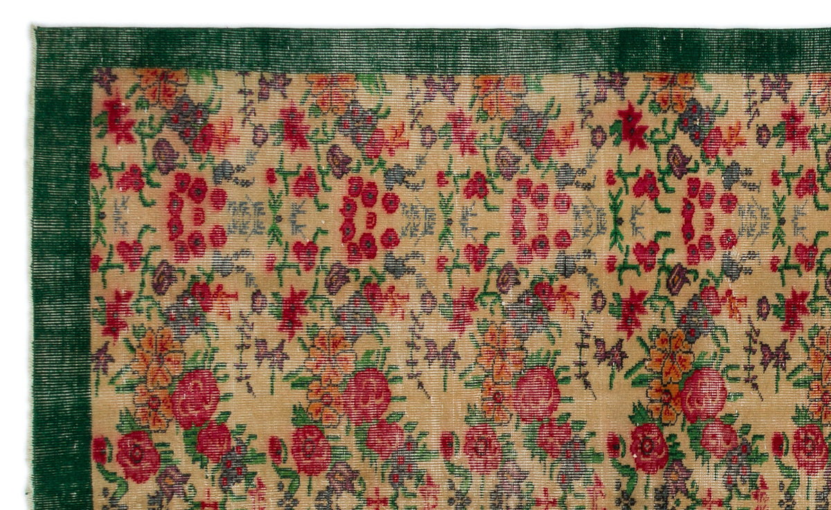 Tan rug with a repeating floral pattern in red, orange, and purple, featuring a solid dark green border.
