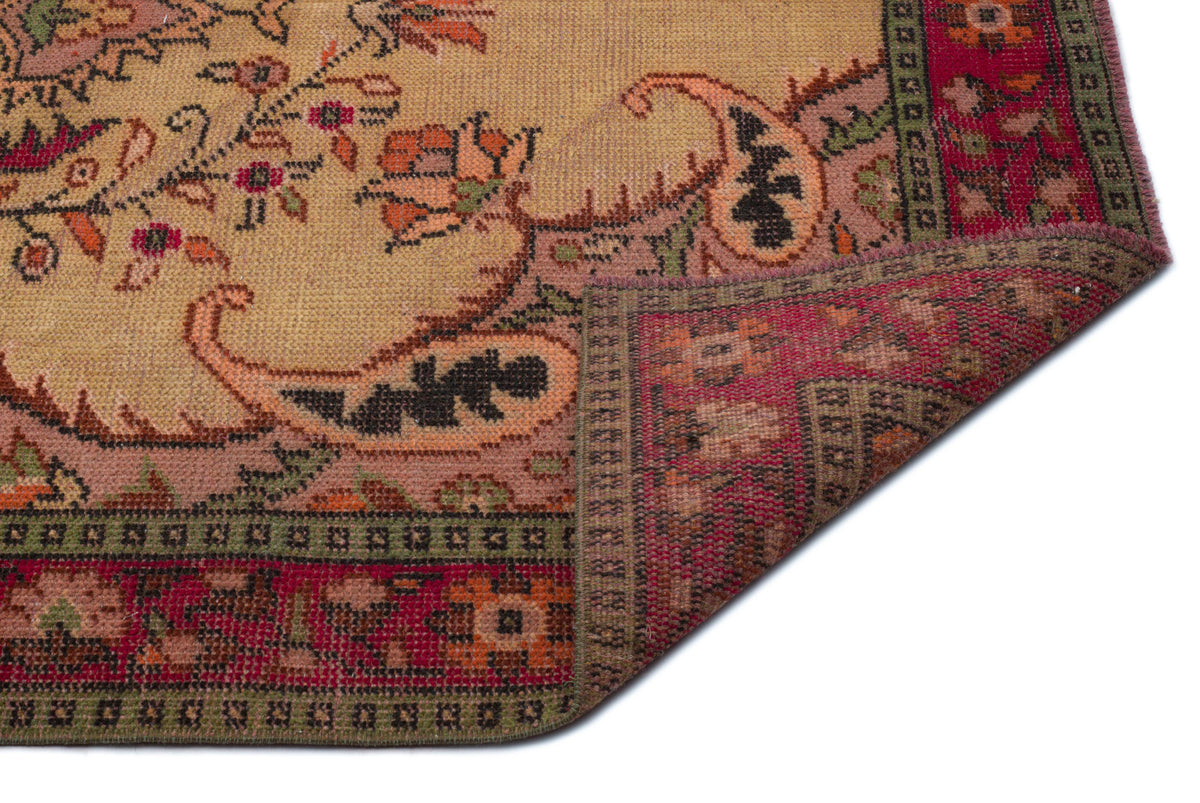 Tan vintage rug with a floral paisley pattern and a red border, shown with a corner folded over on a white background.