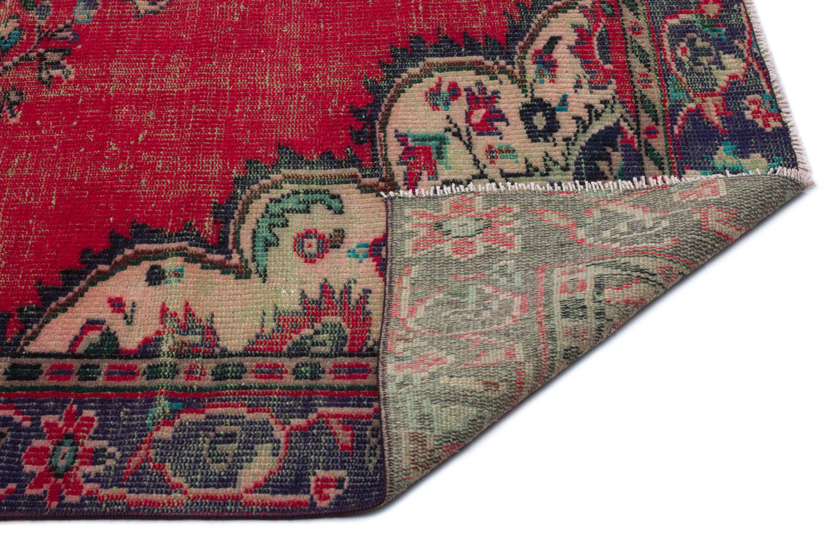 Red vintage-style rug with a floral medallion border and a folded corner revealing the muted green underside.