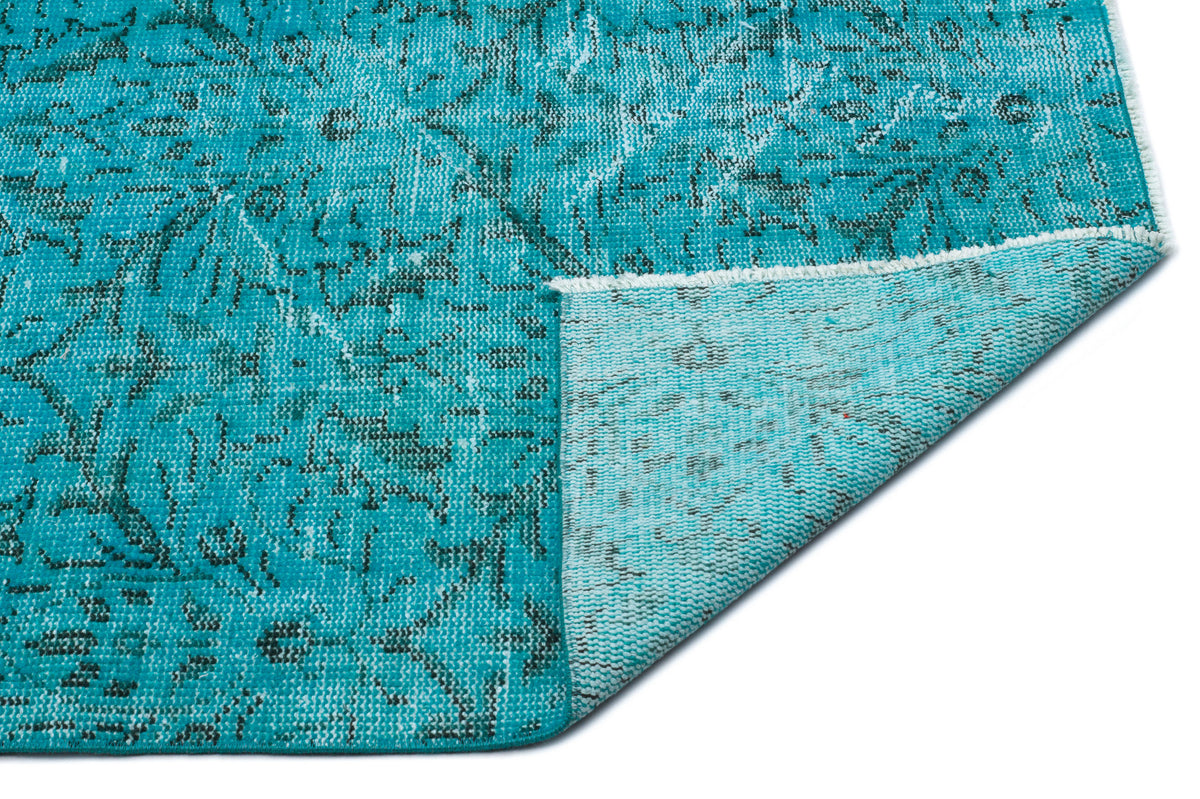 Turquoise and black distressed floral medallion rug with a folded corner showing the woven backing.