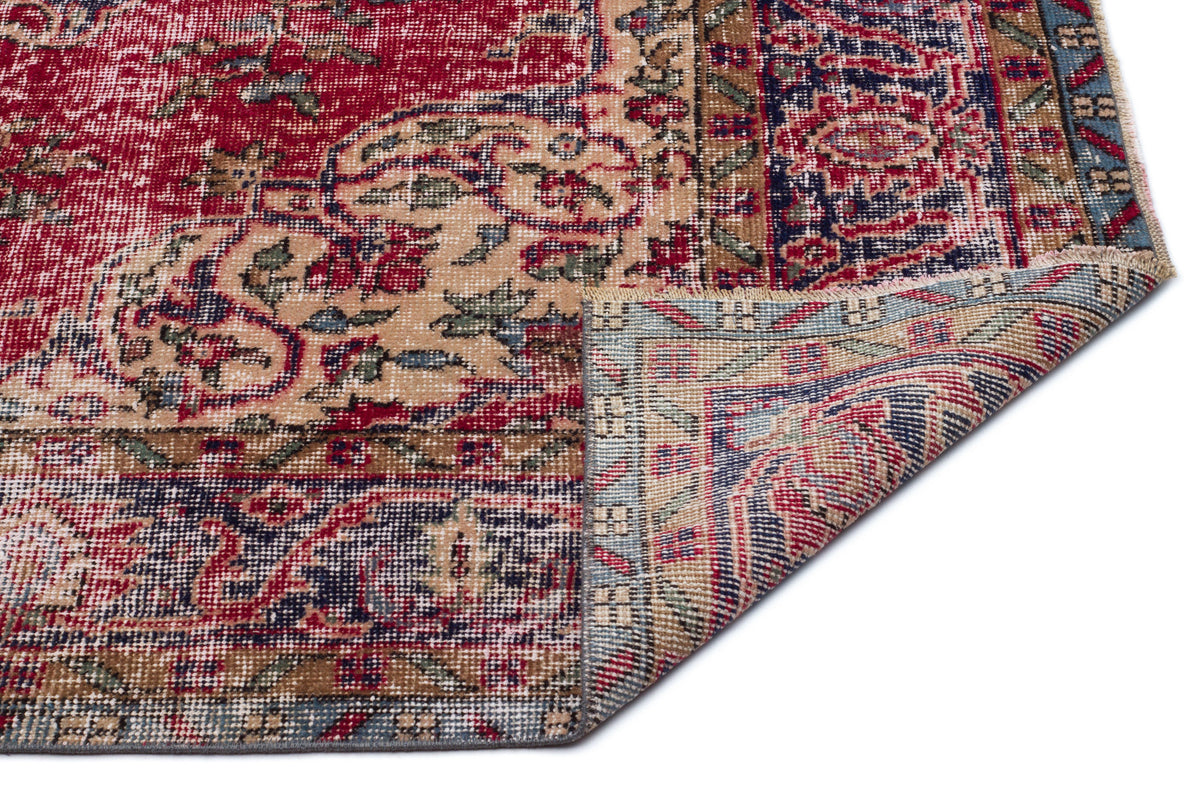 Red, blue, and beige traditional Persian-style rug with a distressed floral pattern, shown with a corner folded over.
