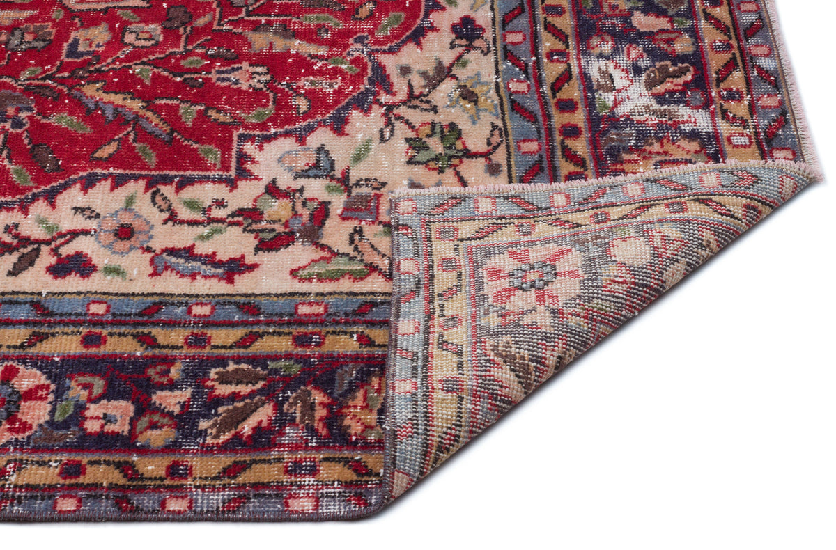 Red, beige, and navy traditional floral rug with a distressed finish, shown with a corner folded over.