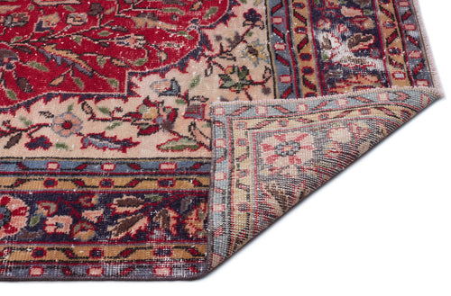 Load image 1 in gallery view. Red, beige, and navy traditional floral rug with a distressed finish, shown with a corner folded over.
