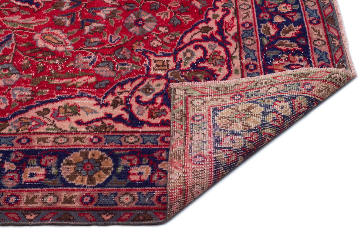 Red and navy blue traditional Persian-style rug with a floral medallion pattern and a folded corner on a white background.