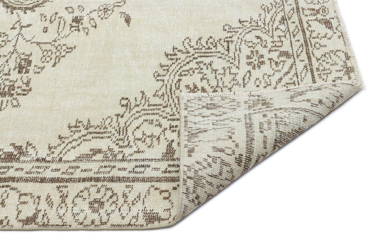 Cream and taupe rug with a distressed traditional medallion pattern, shown with a corner folded over on a white background.