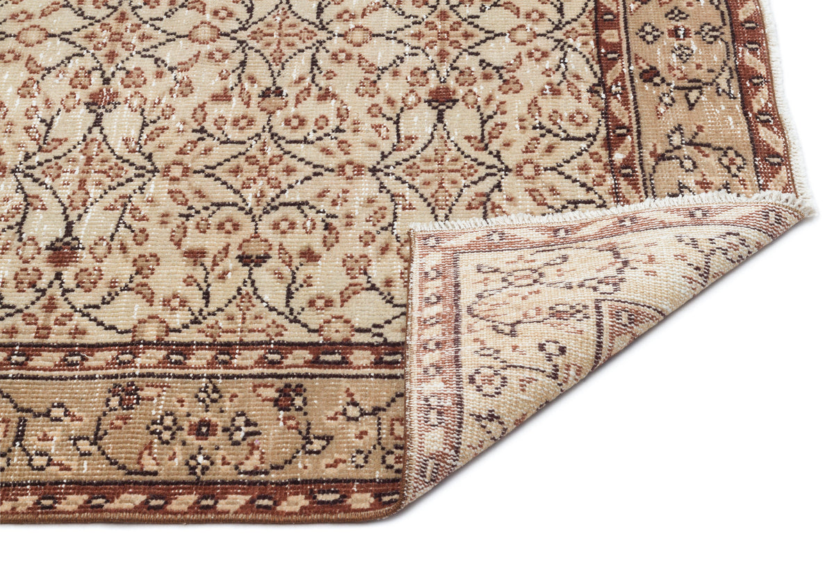 Beige and brown traditional rug with a floral medallion pattern and a folded corner showing the underside.