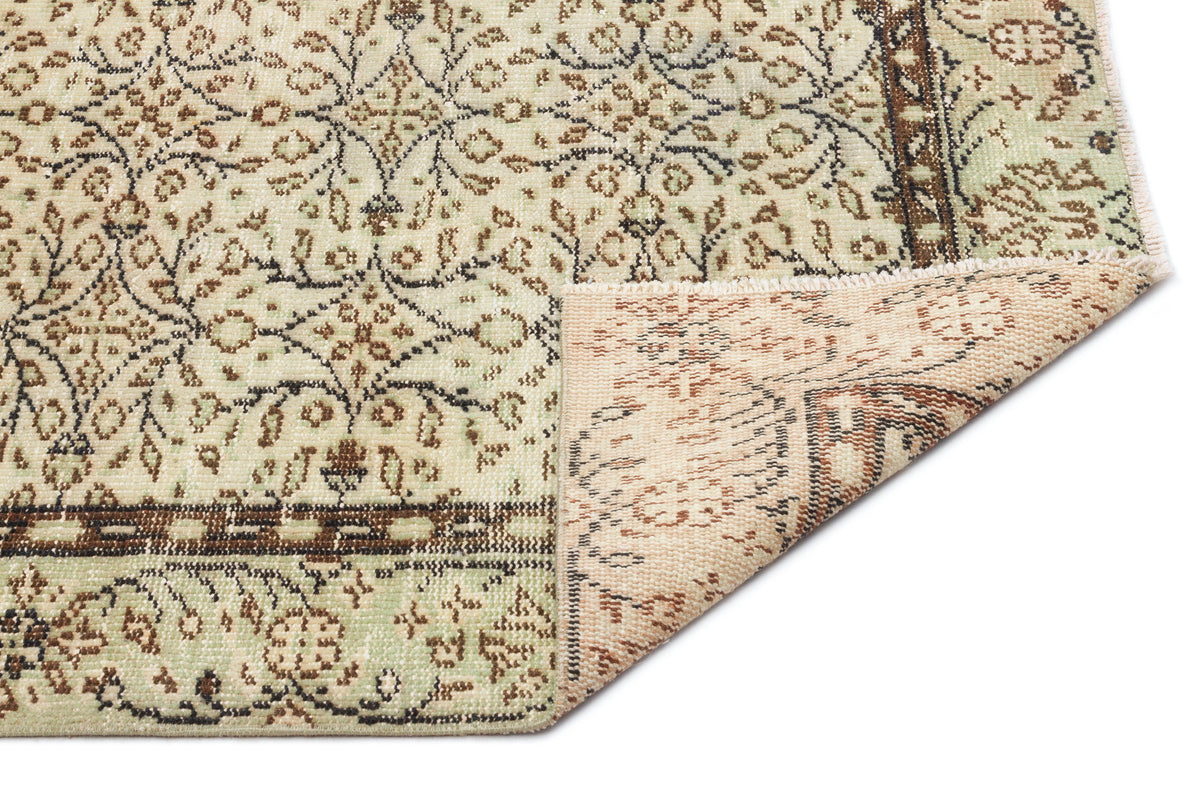 Sage green and brown traditional floral rug with a folded corner revealing the woven backing.