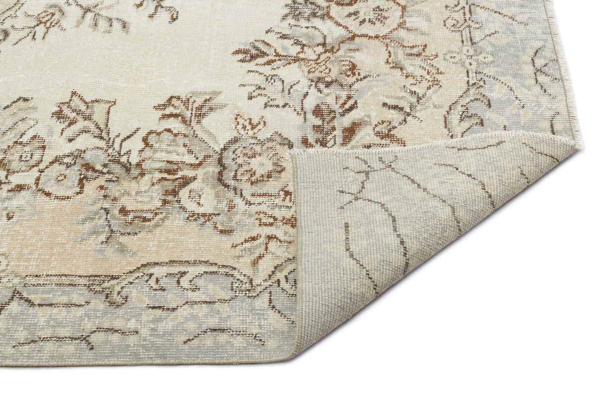 Cream and beige vintage-style rug with a distressed floral pattern and a folded corner showing the woven backing.