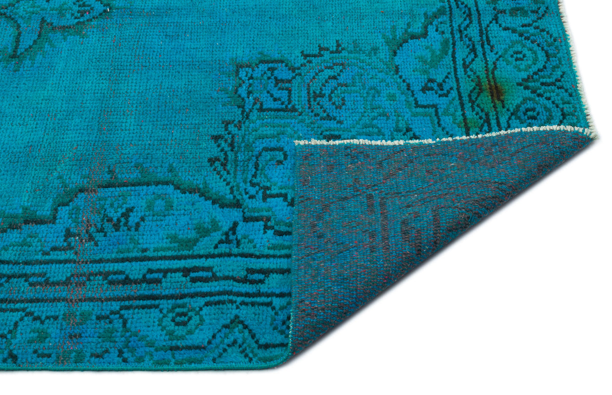 Bright turquoise rug with a dark teal traditional medallion pattern, shown with a corner folded over.