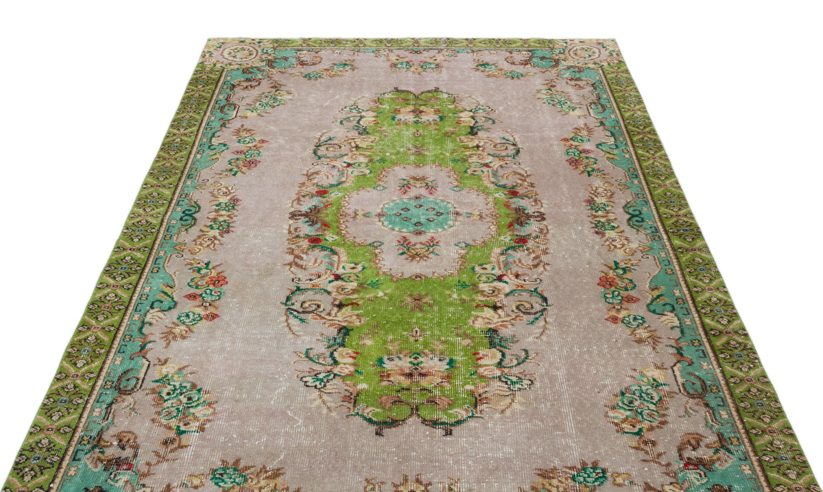 Distressed beige rug with a central green floral medallion and ornate green border on a white background.