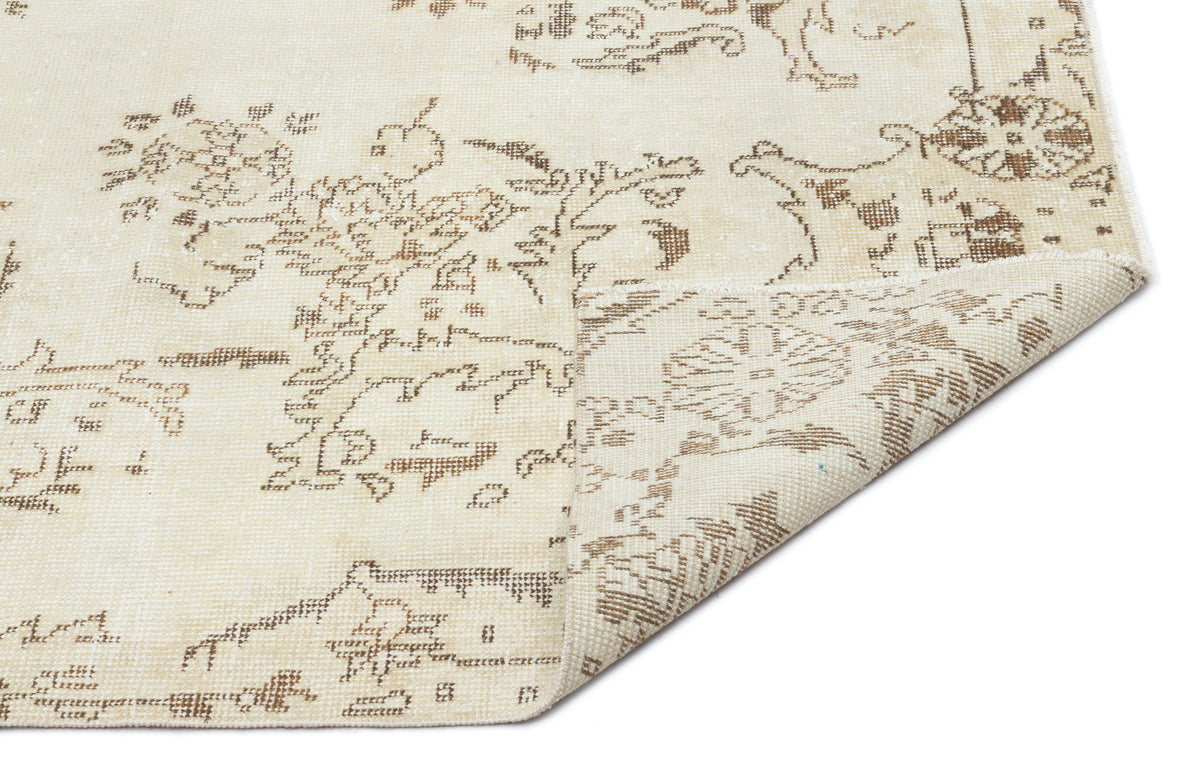 Cream and beige rug with a distressed floral medallion pattern, shown with a corner folded over on a white background.