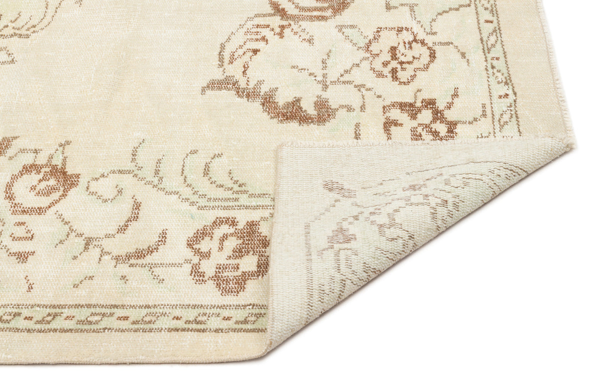 Cream rug with a distressed brown floral pattern and a folded corner showing the woven backing.