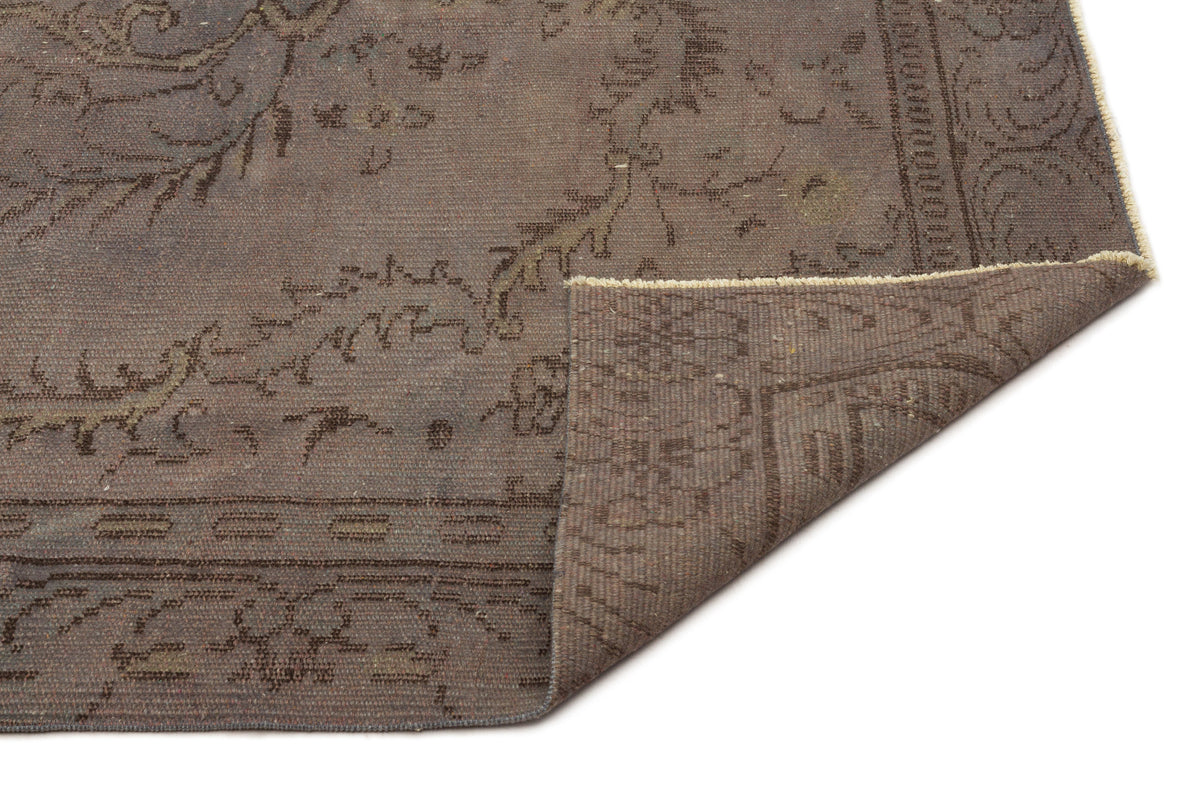 Dark brown distressed rug with a faded traditional floral medallion pattern and a folded corner showing the underside.