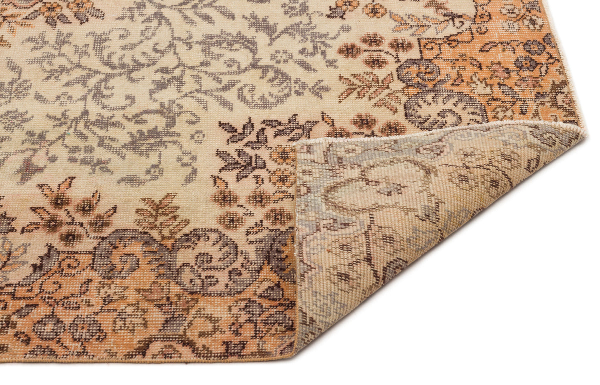 Beige and orange vintage-style rug with a distressed floral pattern and a folded corner showing the woven backing.