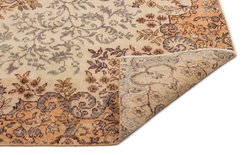 Load image 1 in gallery view. Beige and orange vintage-style rug with a distressed floral pattern and a folded corner showing the woven backing.