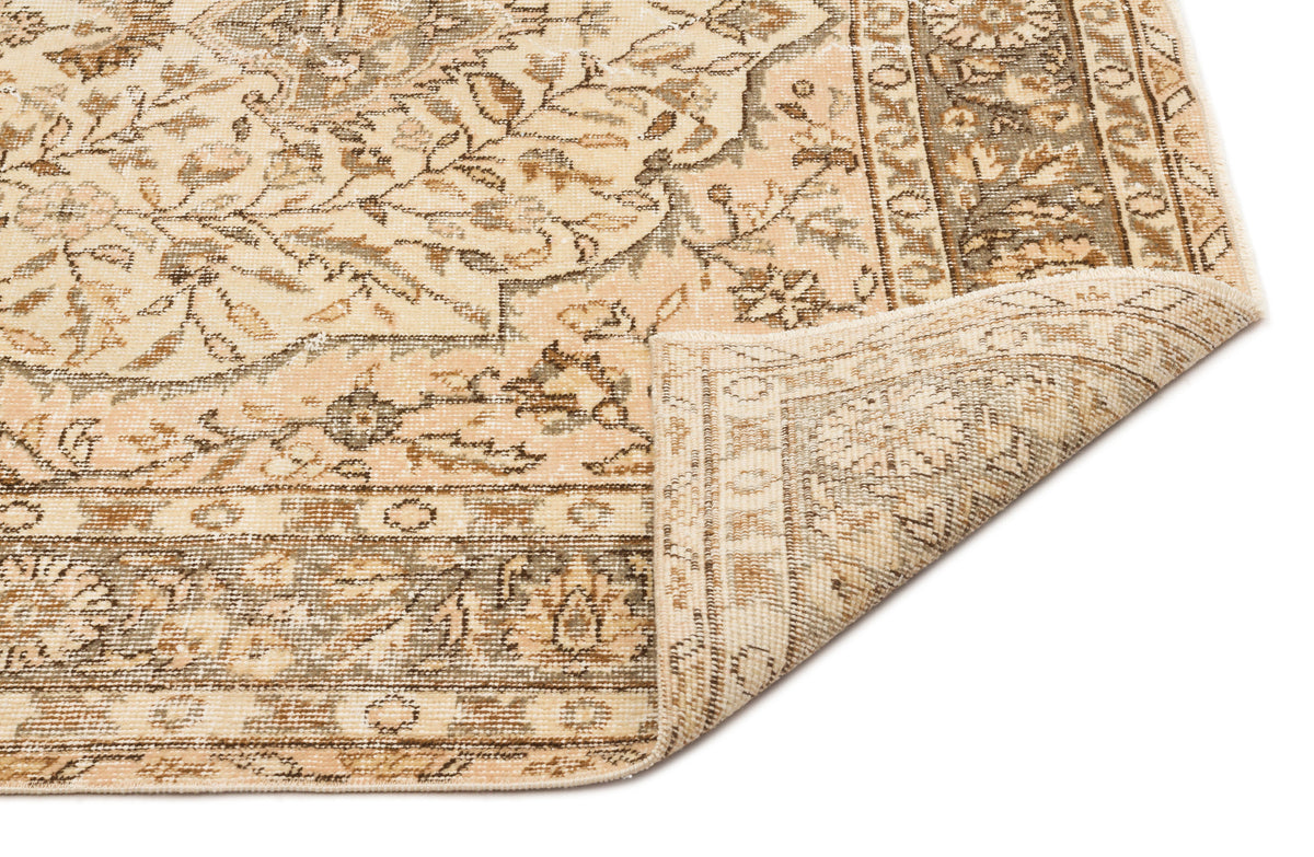 Beige and brown traditional floral rug with a folded corner revealing the woven backing on a white background.