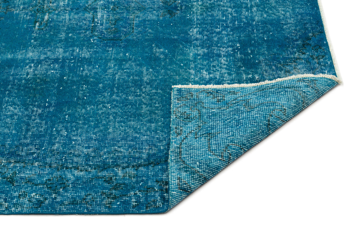 Teal distressed rug with a faded traditional pattern and a folded corner showing the woven backing.