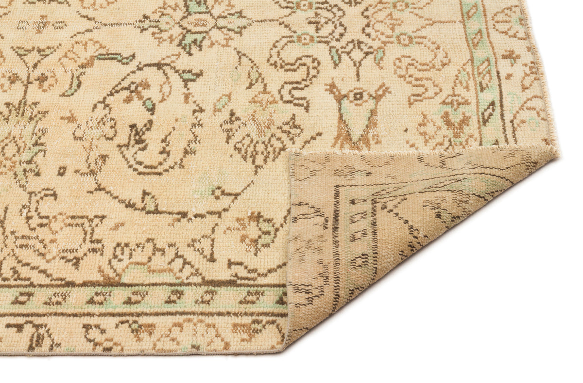 Beige and brown traditional rug with a faded floral medallion pattern and a folded corner, isolated on white.
