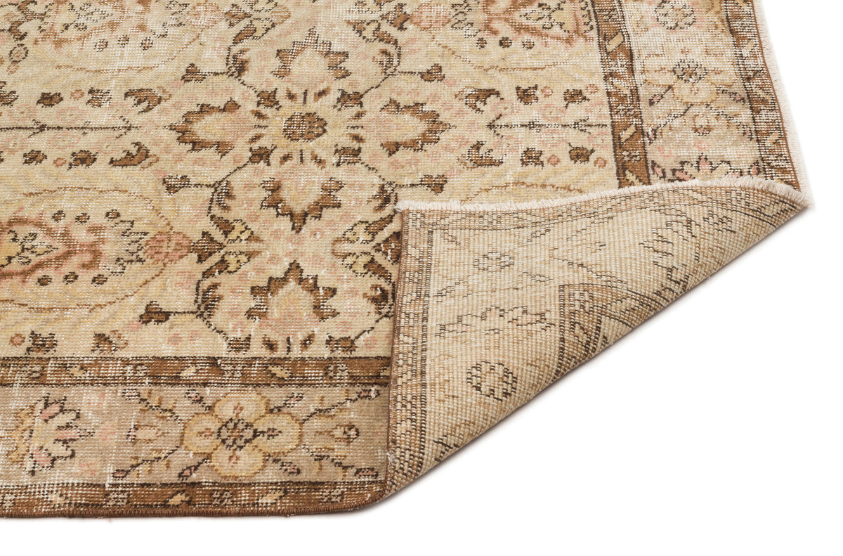 Beige and brown vintage-style rug with a floral medallion pattern and a folded corner showing the woven backing.