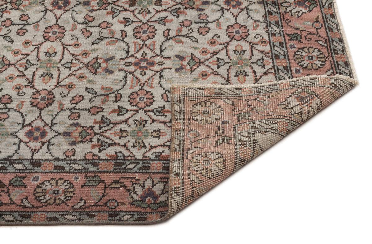 Distressed floral medallion rug in cream, dusty pink, and sage green with a folded corner showing the woven backing.