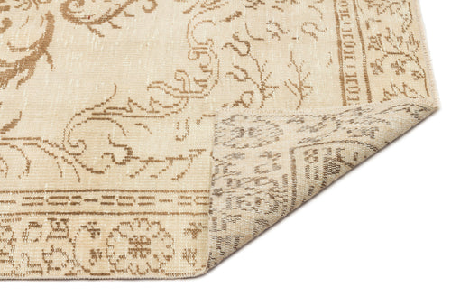 Load image 1 in gallery view. Beige and tan rug with a faded traditional floral pattern, shown with a corner folded to reveal the woven backing.