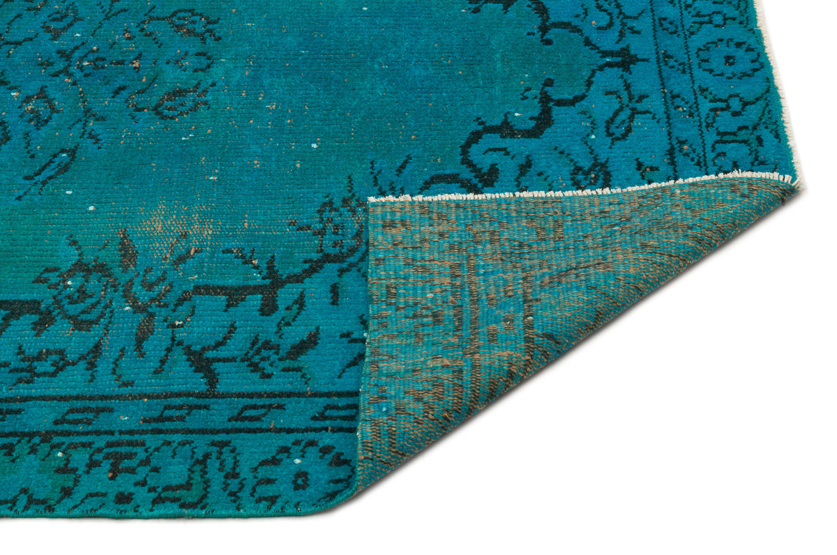 Teal and black distressed traditional rug with a folded corner revealing a brown woven backing on a white background.