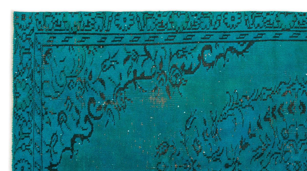 Teal rug with a distressed black floral medallion pattern and a geometric border.