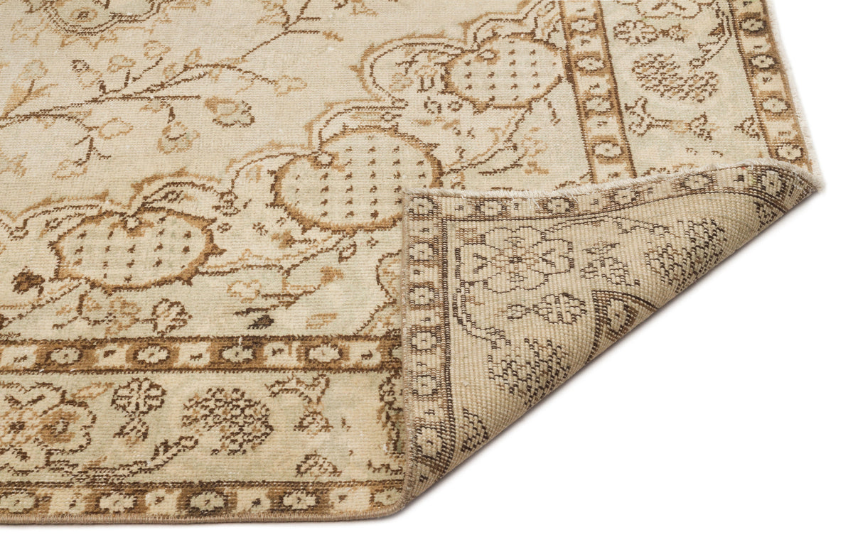 Beige and brown traditional floral medallion rug with a folded corner on a white background.