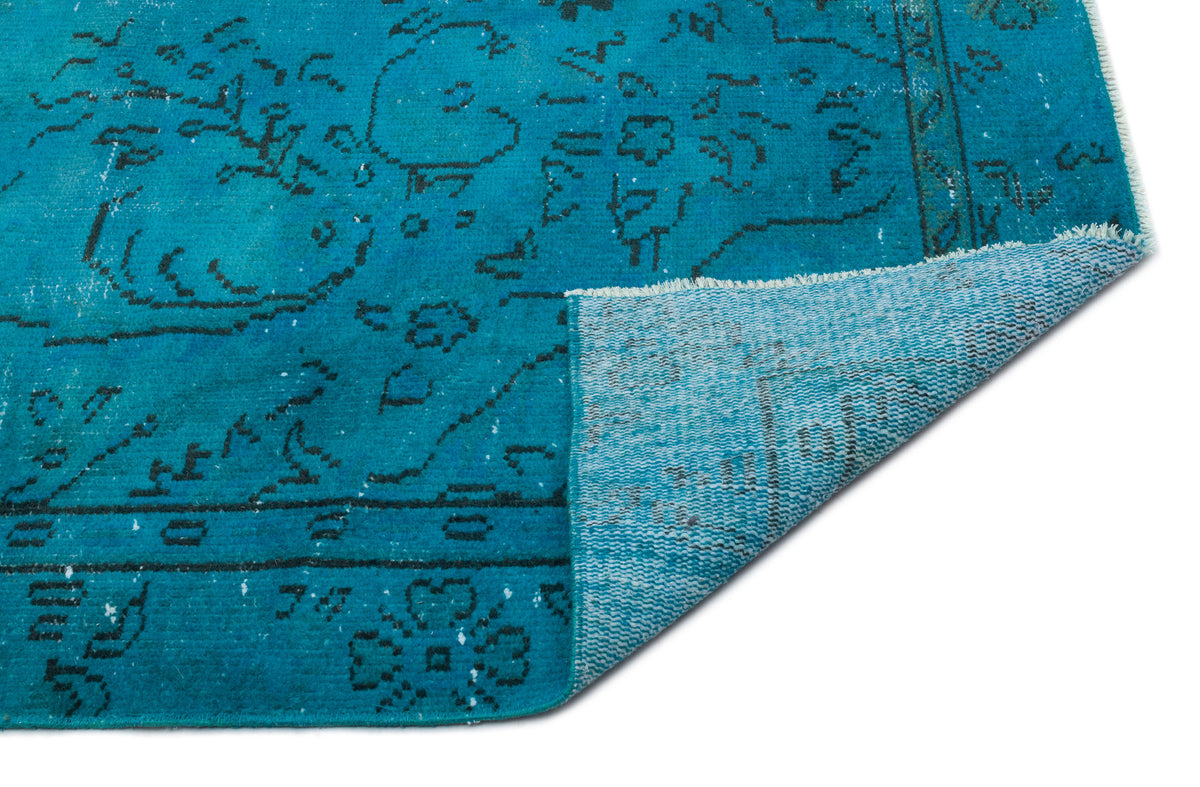 Teal distressed rug with a black floral medallion pattern, shown with a folded corner on a white background.