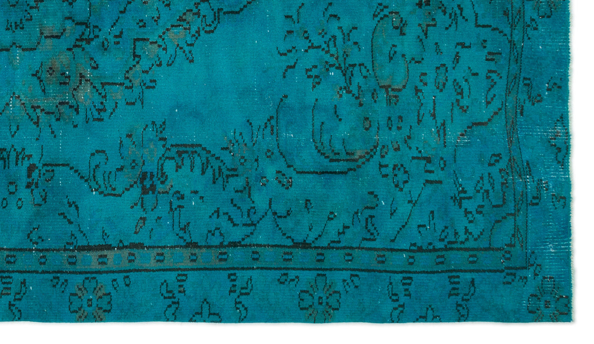 Teal rug with a distressed black floral pattern and a geometric border on a white background.