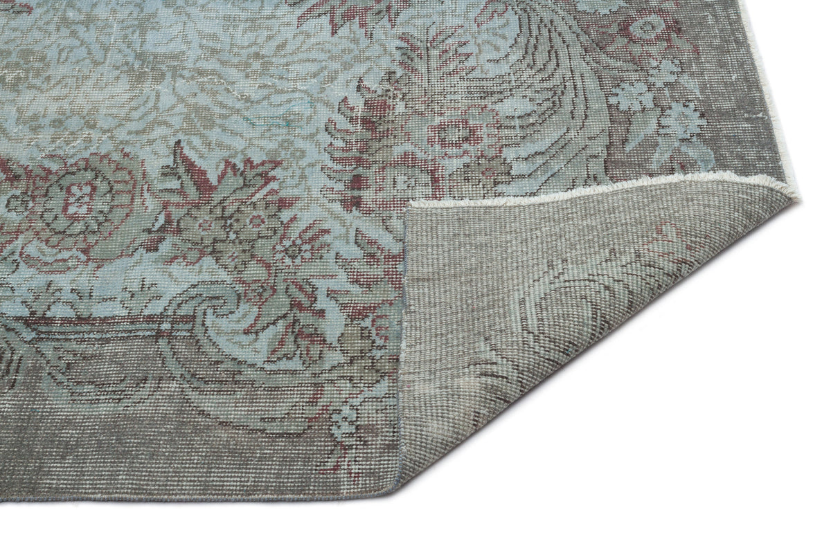 Light blue and grey traditional floral medallion rug with a distressed finish, shown with a corner folded over.