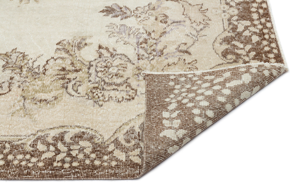 Beige and brown vintage-style rug with a faded floral medallion pattern and a folded corner showing the reverse side.