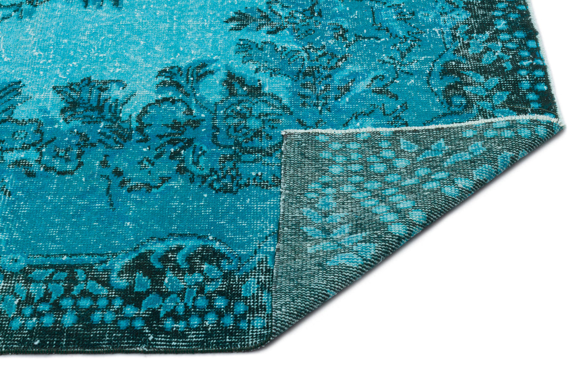 Bright turquoise and dark teal distressed rug with a floral medallion pattern, shown with a corner folded over.