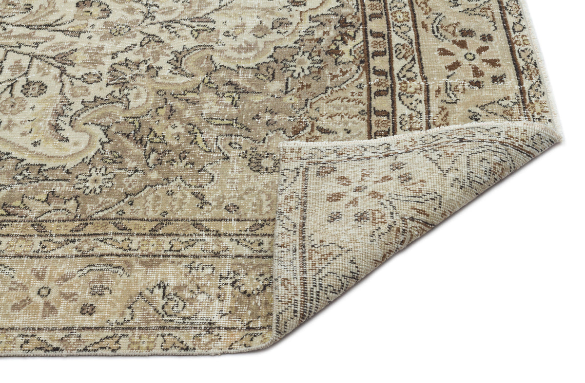 Beige and brown vintage-style rug with a distressed floral pattern and a folded corner, isolated on a white background.