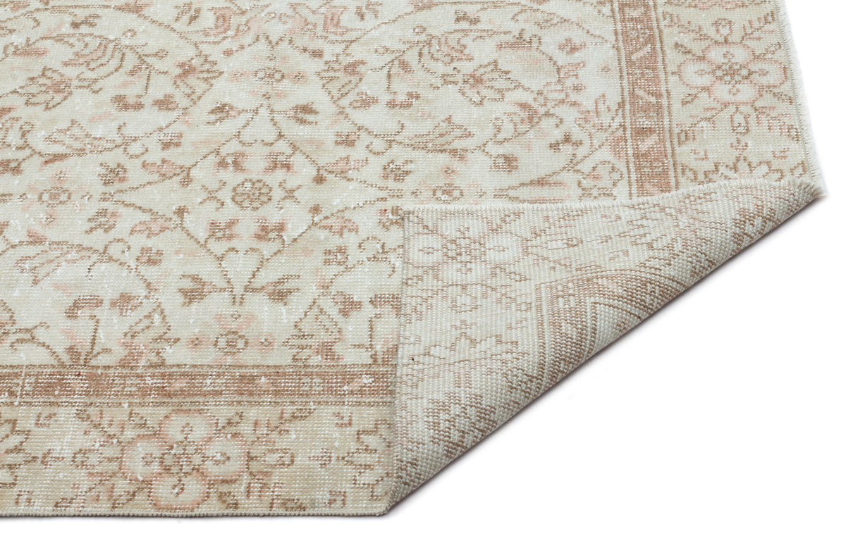 Cream and beige rug with a distressed floral medallion pattern and a folded corner, isolated on a white background.