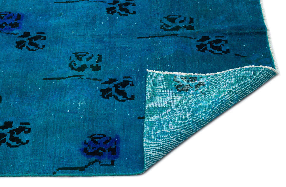 Bright blue rug with a distressed black floral pattern and a folded corner revealing a light blue woven backing.